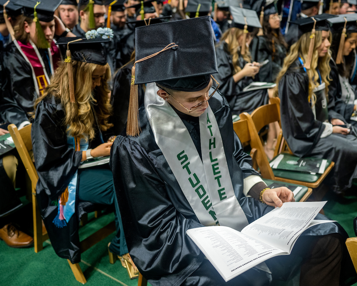 Graduate wearing student athlete mantle examines graduation program