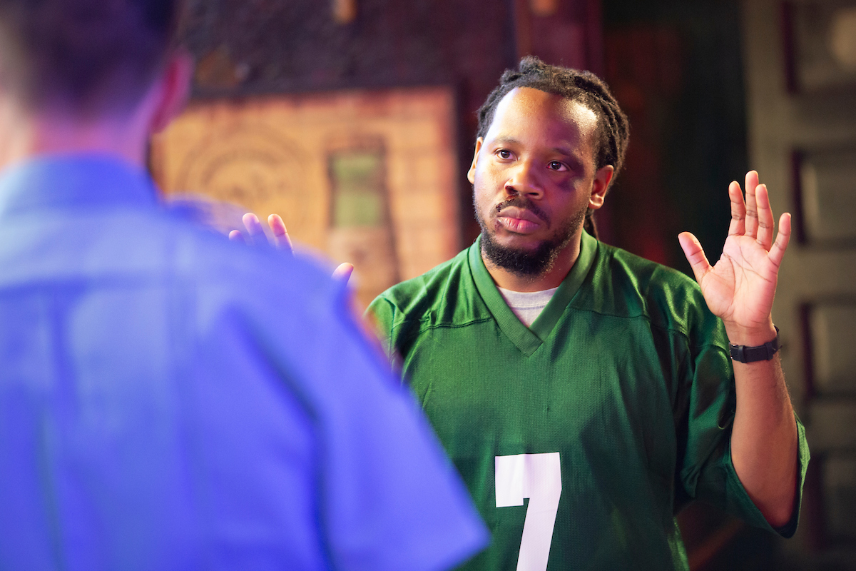 An actor portraying a protester raises his arms to show a castmate playing a police officer he is not a threat