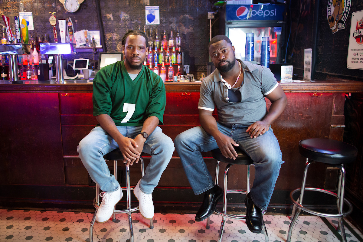 Actors Brandyn Bailey and LeJon Woods sit in front of a bar set.
