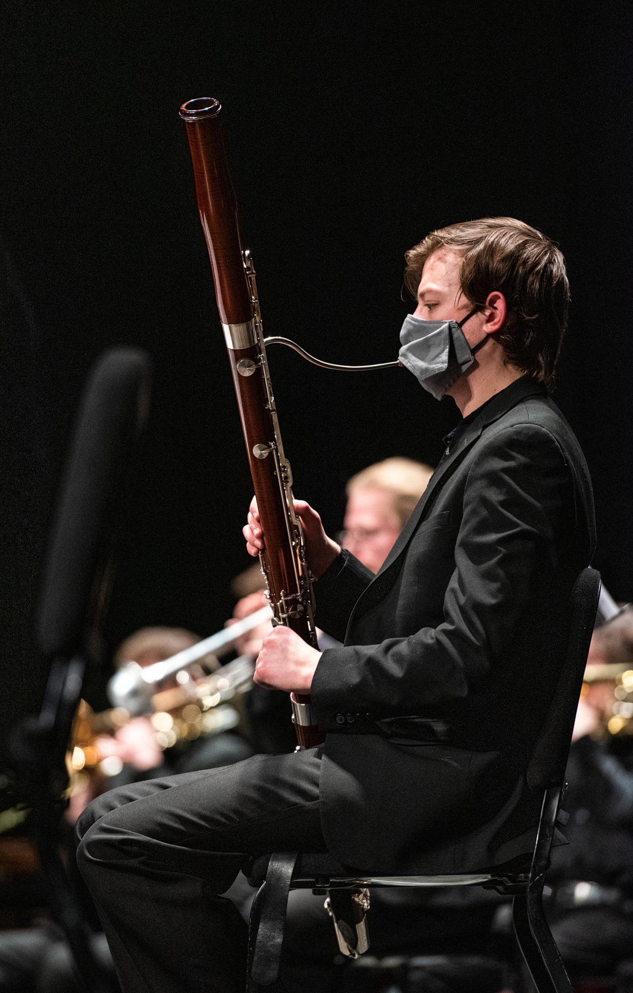 A symphony member attempts to play a woodwind through a mask