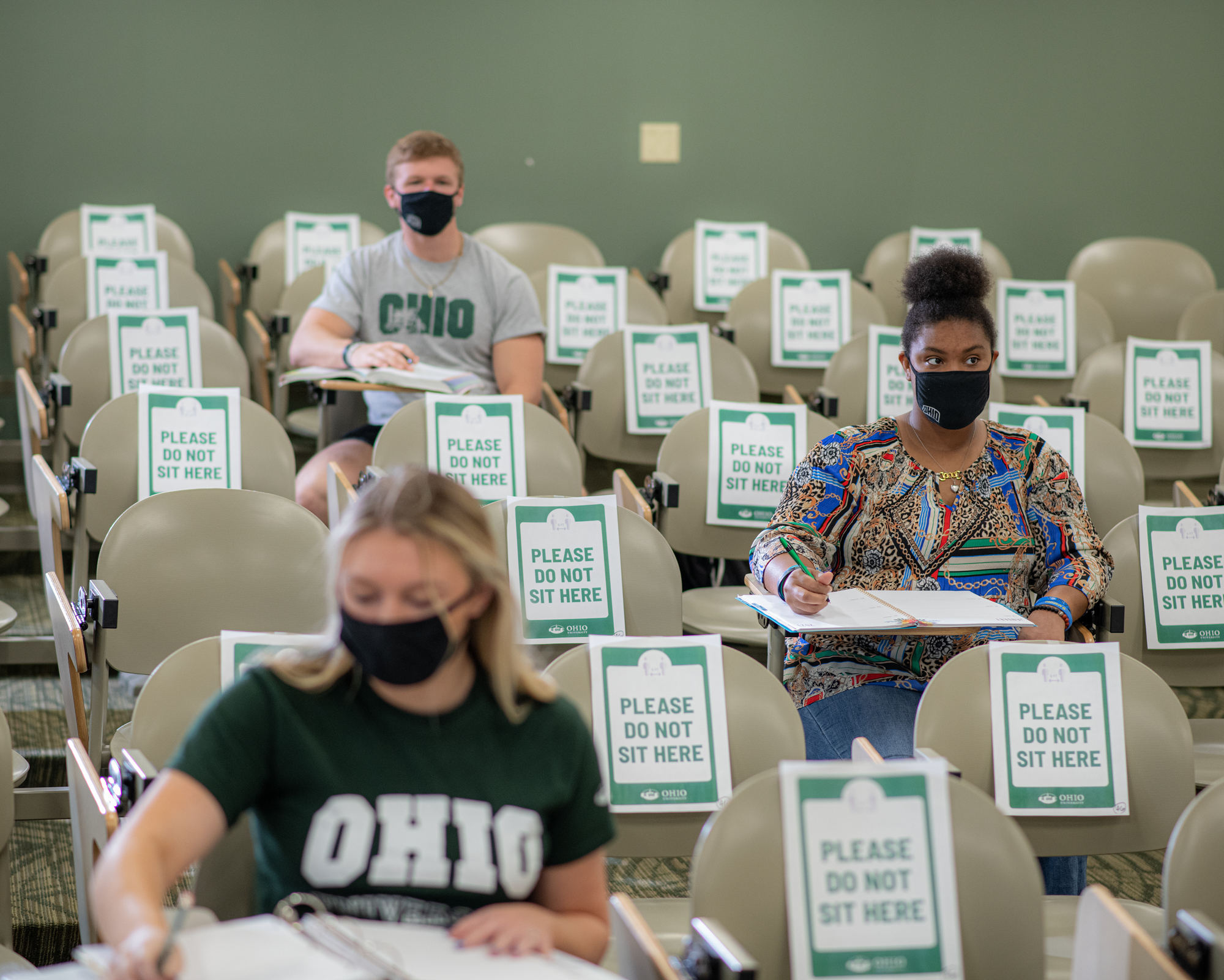 Students sitting in a sparsely attended lecuture hall wearing masks