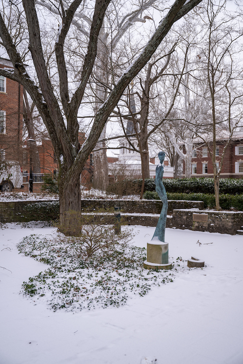 A statue of a woman's figure beneath a tree, with snow covering the ground