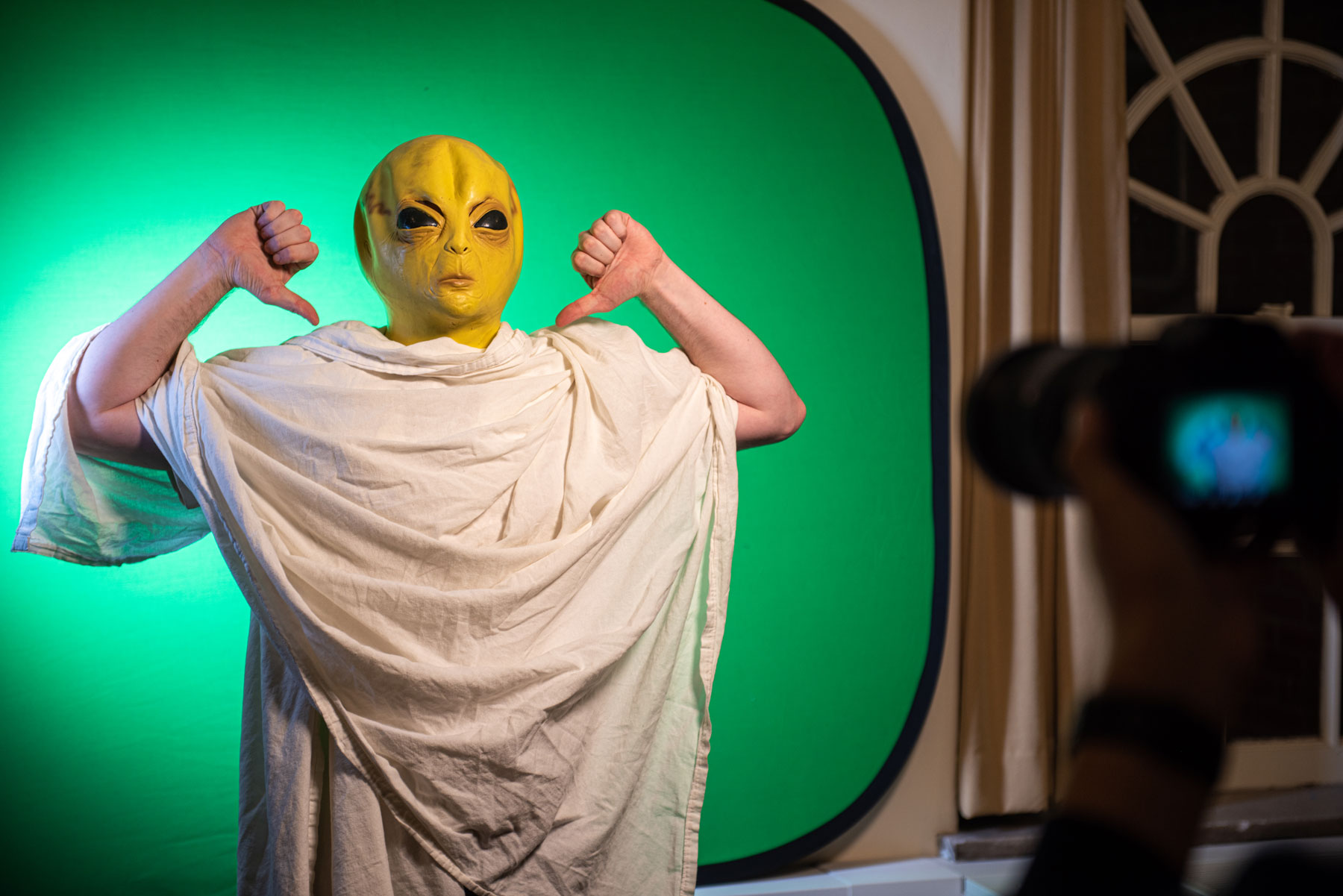 A person in an alien mask poses in front of a video green screen