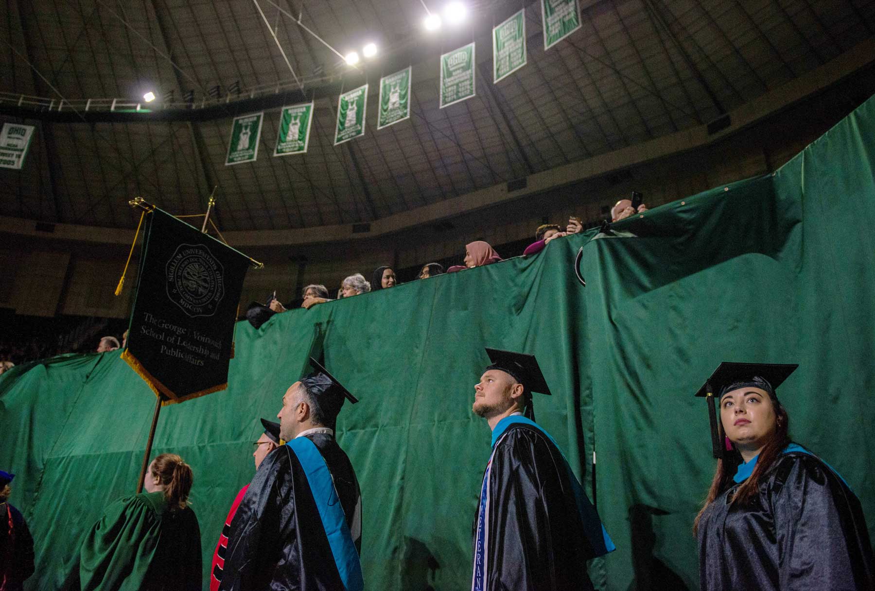 Photo of students walking in cap and gown inside convocation center.