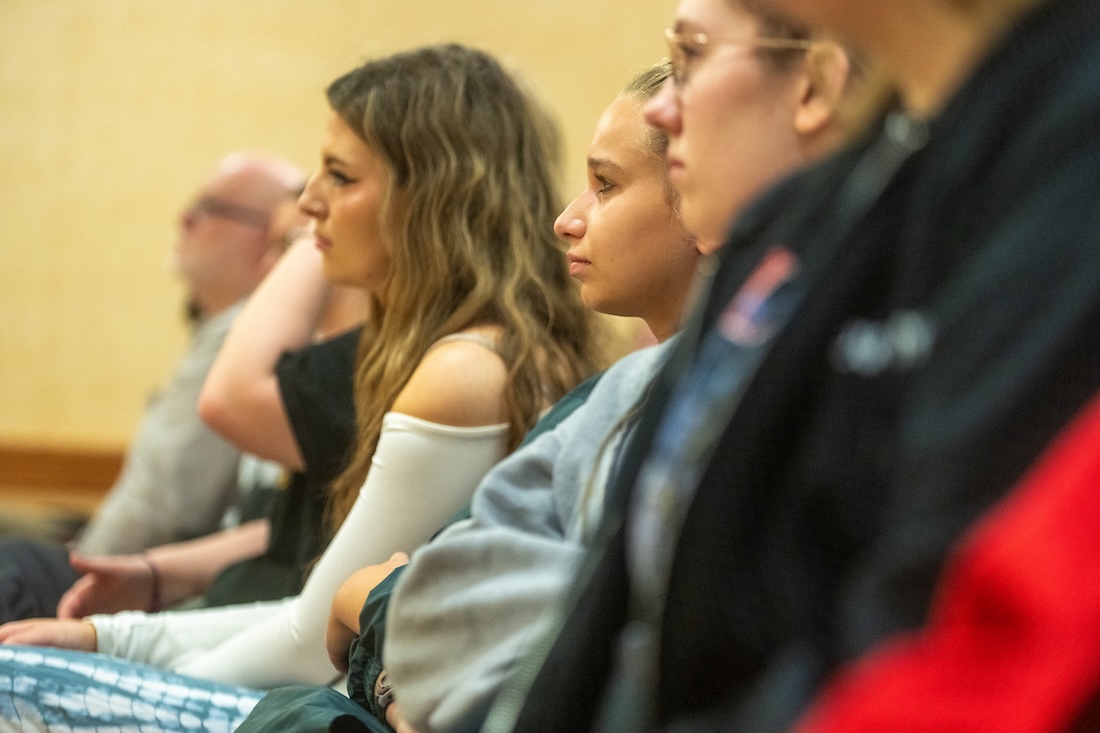 A student sits in an audience, listening intently to a speaker