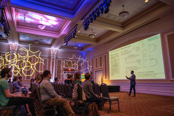 A presenter stands in front of an audience