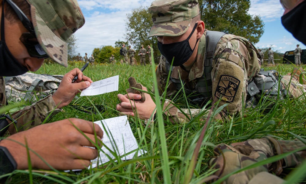 army men in uniform wearing COVID-19 maks. Laying down in the grass while writing on paper