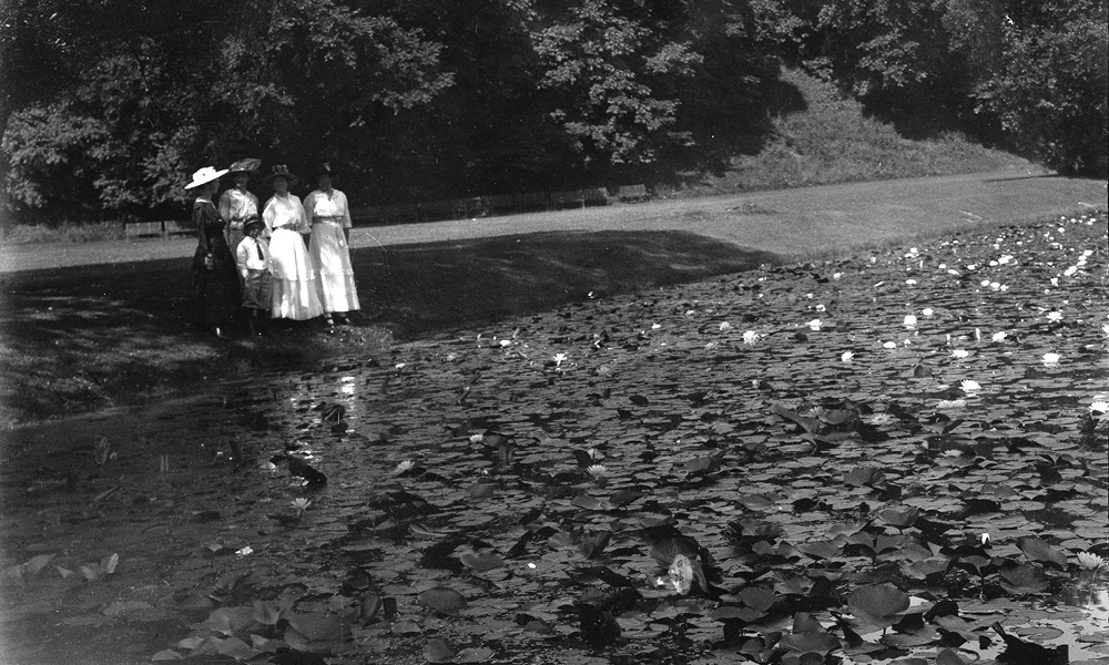 a group of people over looking a pond full of lily pads, black and white photo