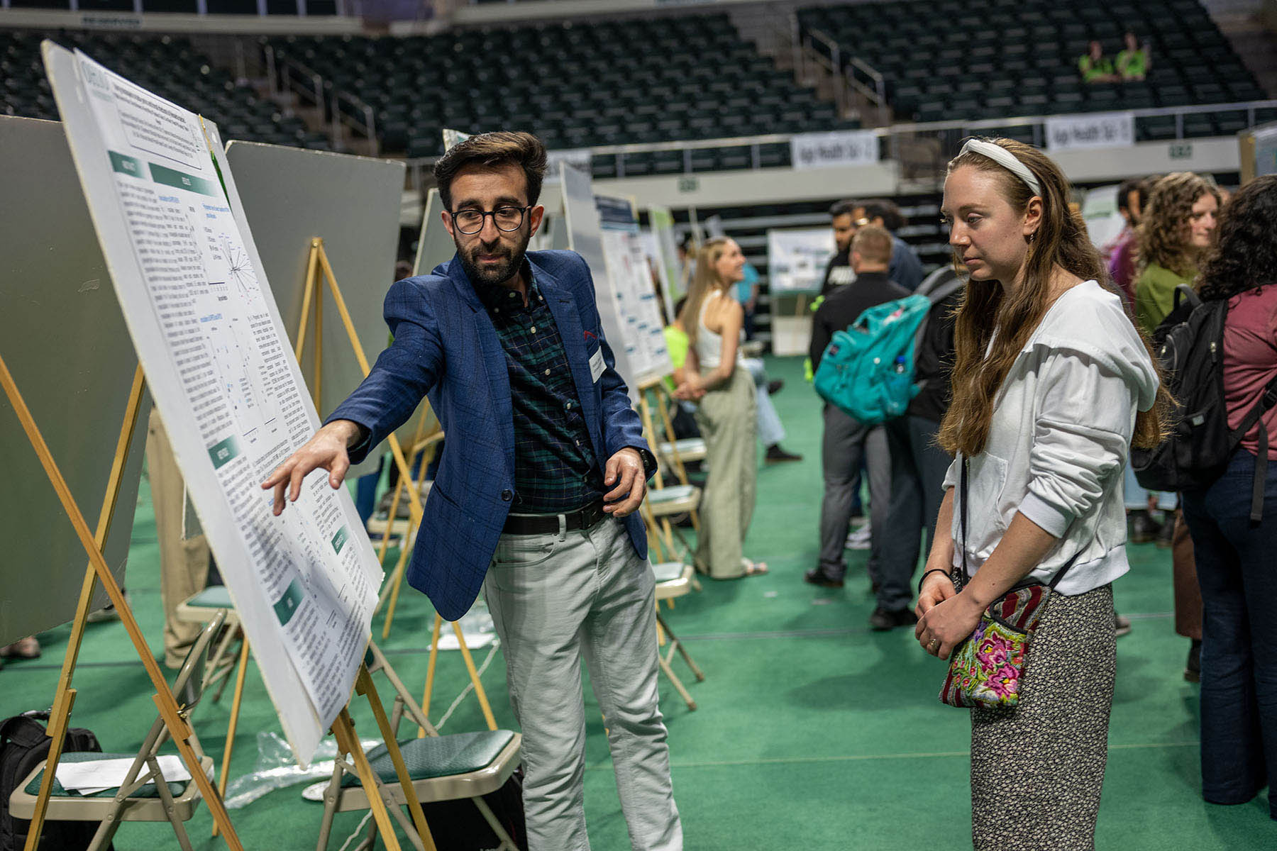 a student points to his research project display while another student looks on