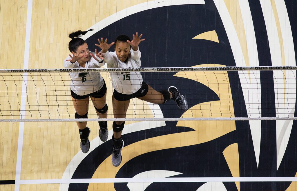 two volleyball players jumping up to the net