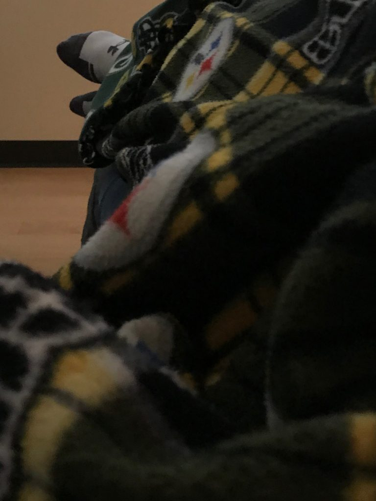 A Pittsburgh Steelers fleece blanket covers a person, but only their feet are visible.