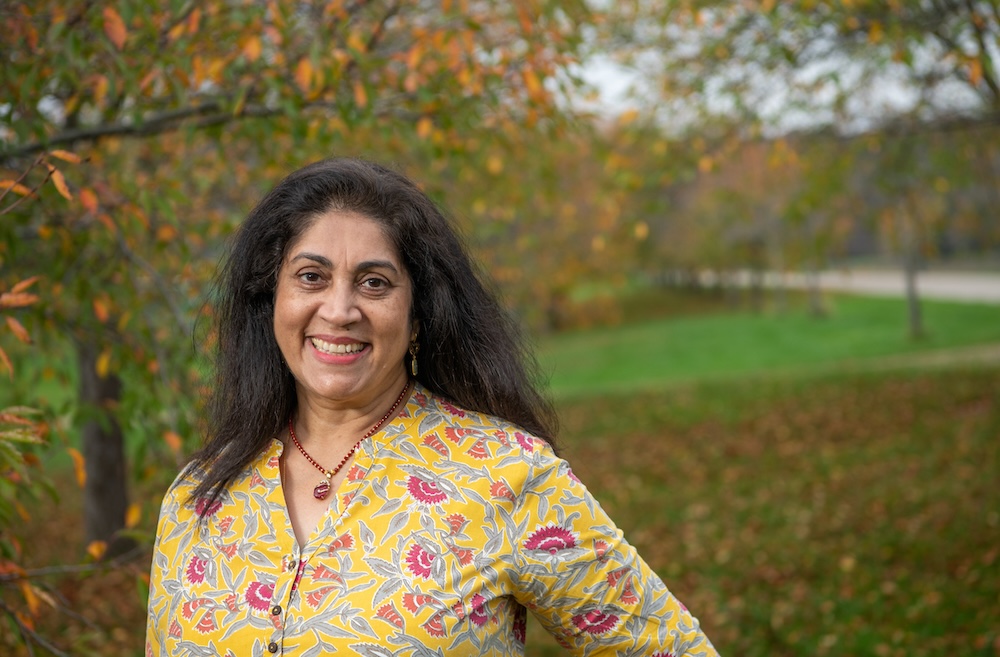 With trees and lawn behind her, Christine Bhat smiles at the camera