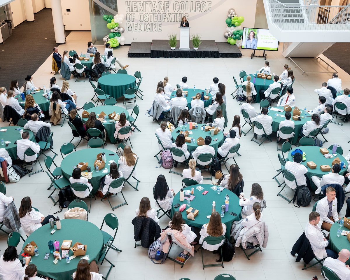 OHIO medical students seated at round tables listen to Dr. Amy Acton speak from the front stage in March 2024.