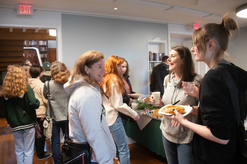 People gather in a breakfast reception, holding plates and chatting