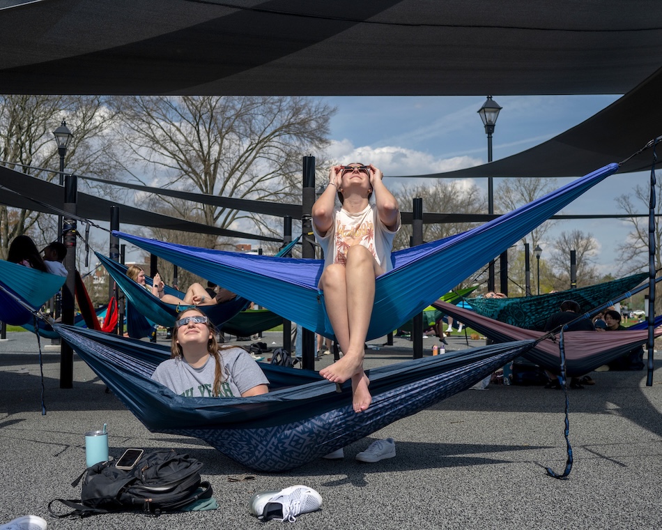Students wearing solar eclipse glasses gaze at the sky from hammocks