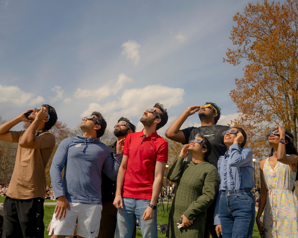 A group of people wearing solar eclipse glasses gaze at the sky