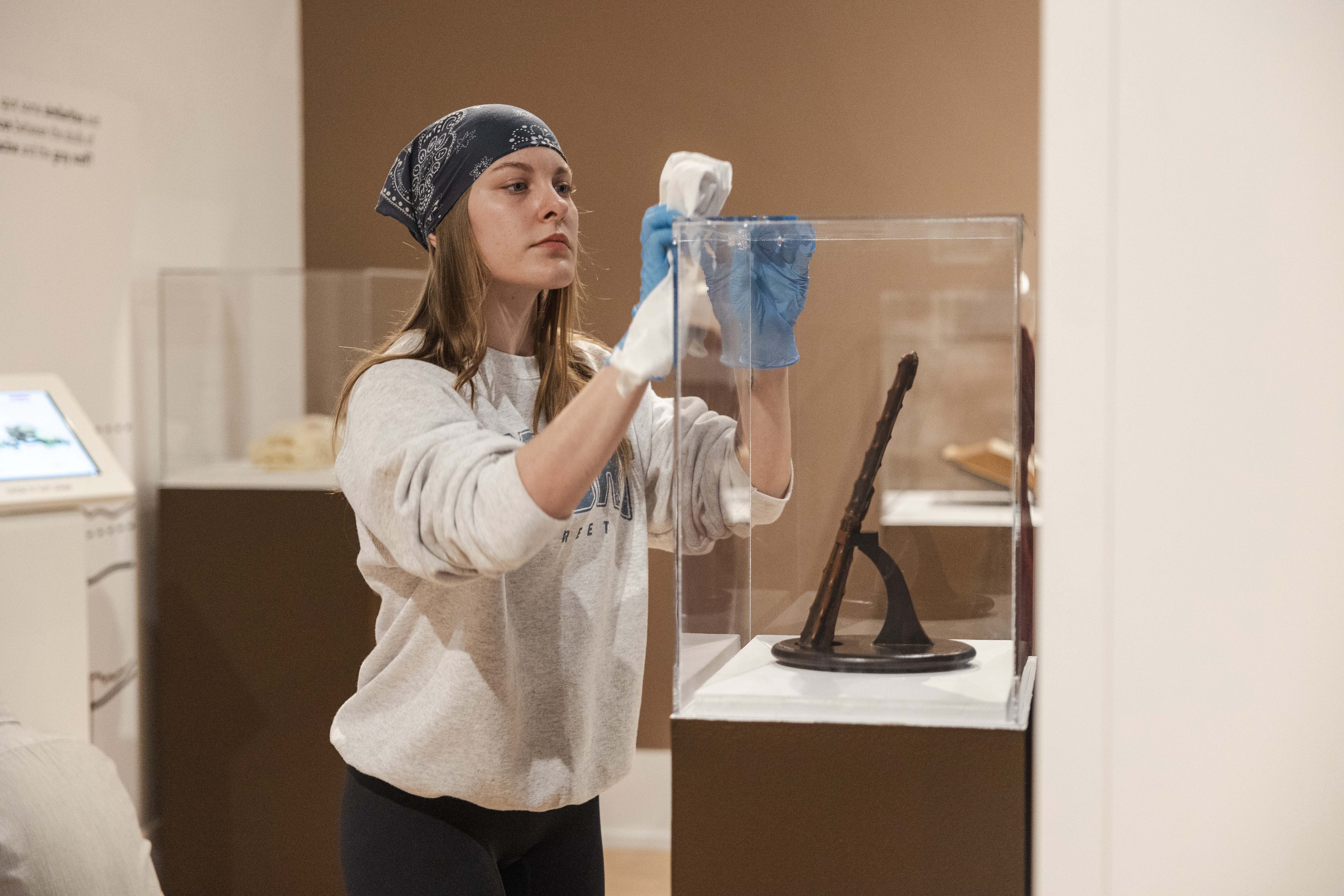 An OHIO Museum Studies Certificate program student wipes the glass of an exhibit.
