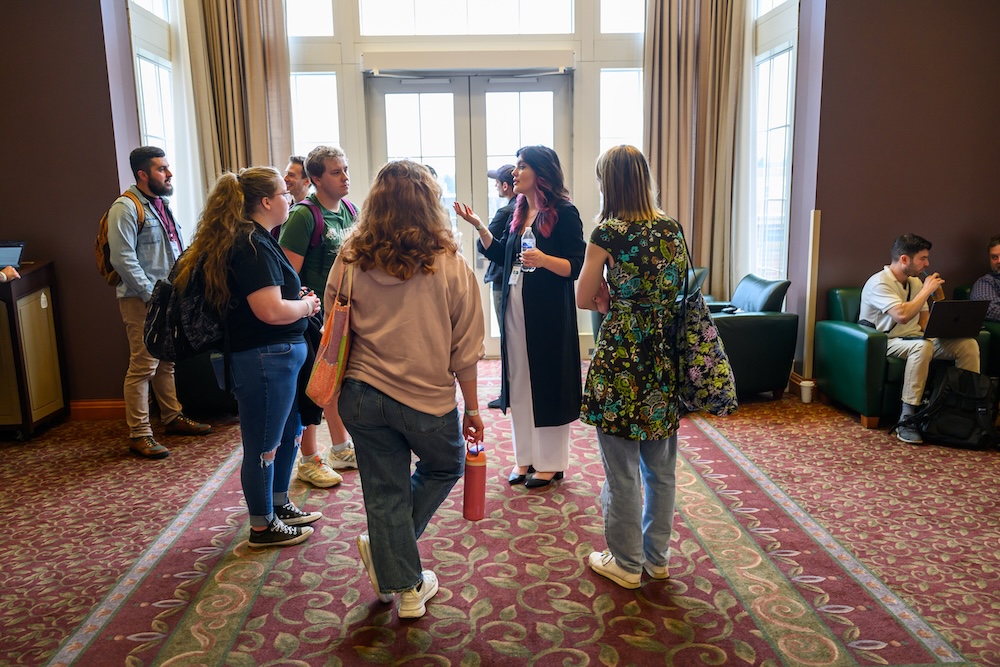 A group of people stand talking in a circle in a sunlit hallway