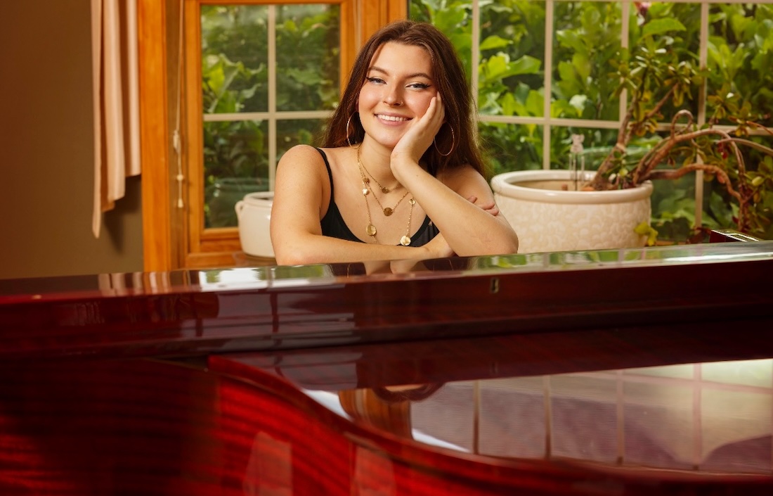Rylie Stopperich poses, seated at a piano with her elbows resting on the top