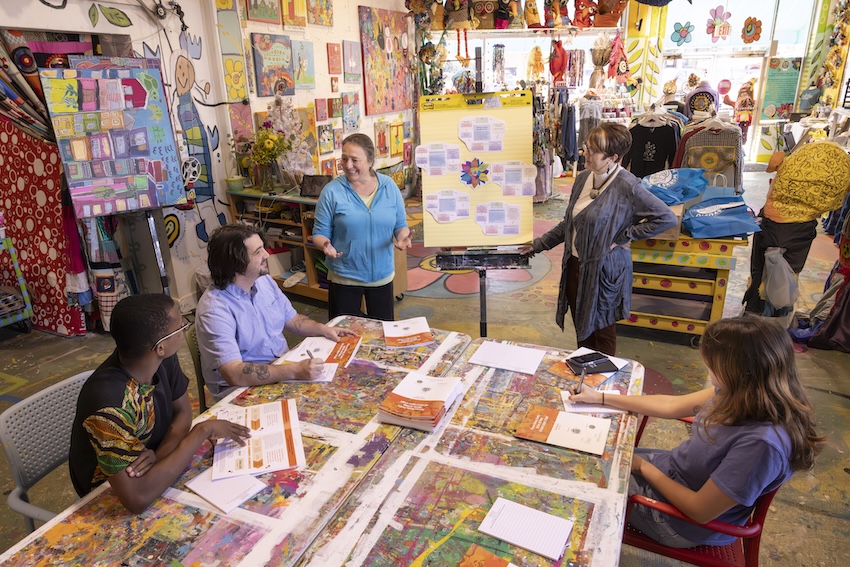 A group of people gather at a conference table, their attention directed toward an easel in front of them