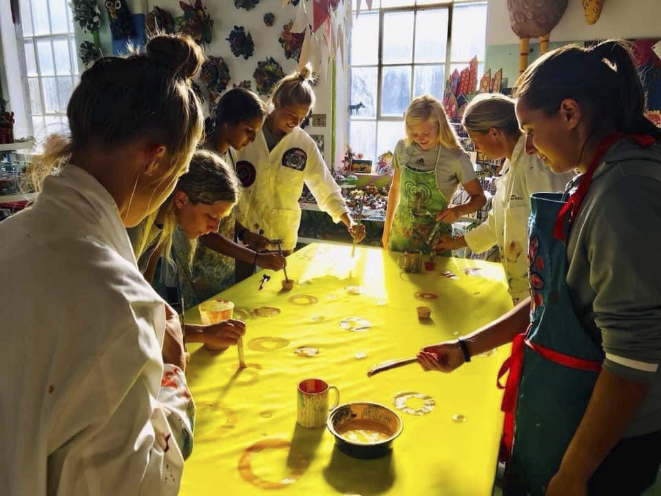 A group of students stand around a table, painting a large yellow mural 