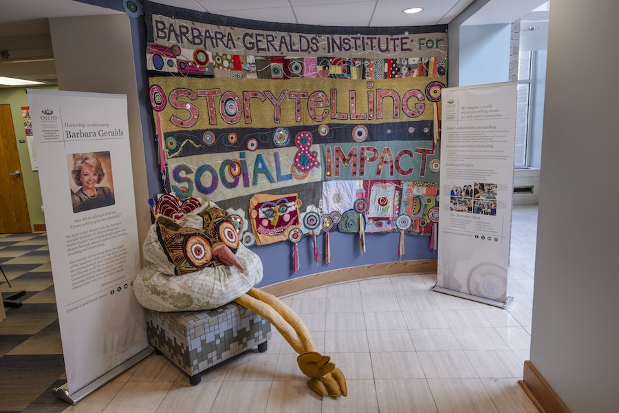 A large, colorful quilt is hung on a wall. It says "The Barbara Geralds Institute for Storytelling & Social Impact"