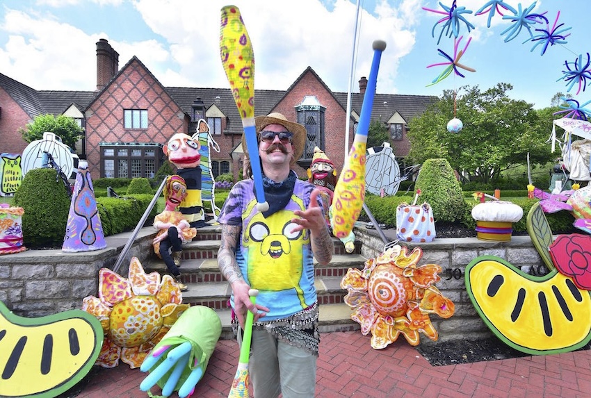 Surrounded by brightly-colored puppets, a man juggles three large colorful items