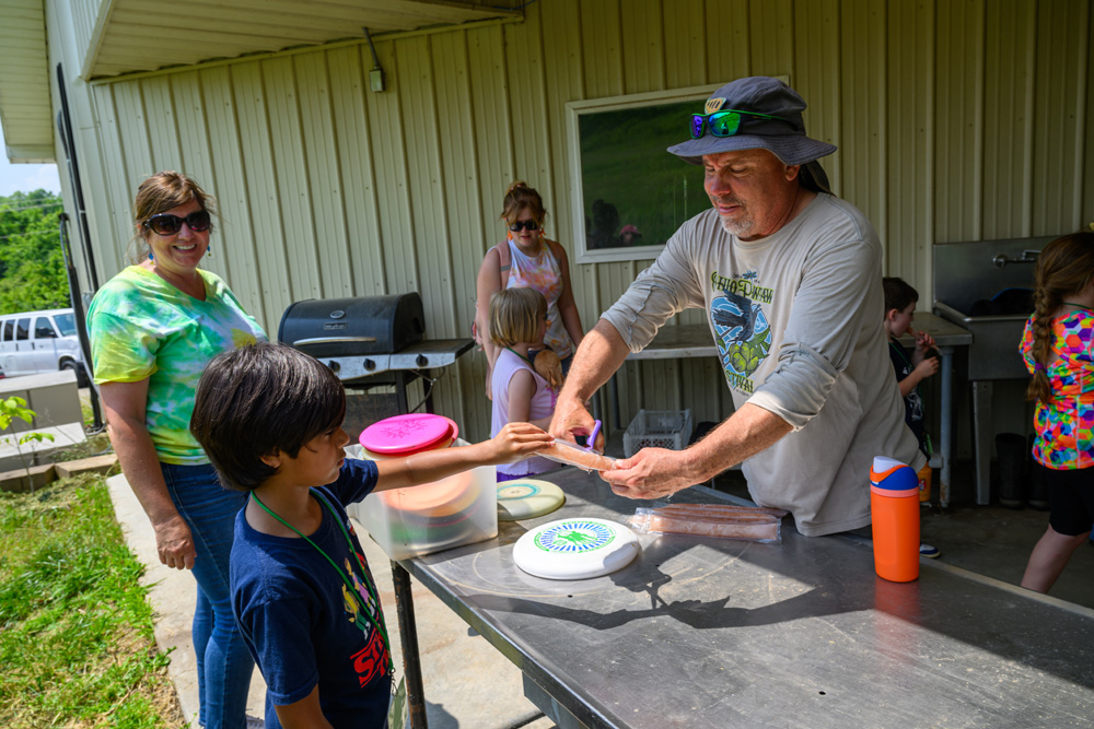 A counselor cutting a popsicle for a camper. 