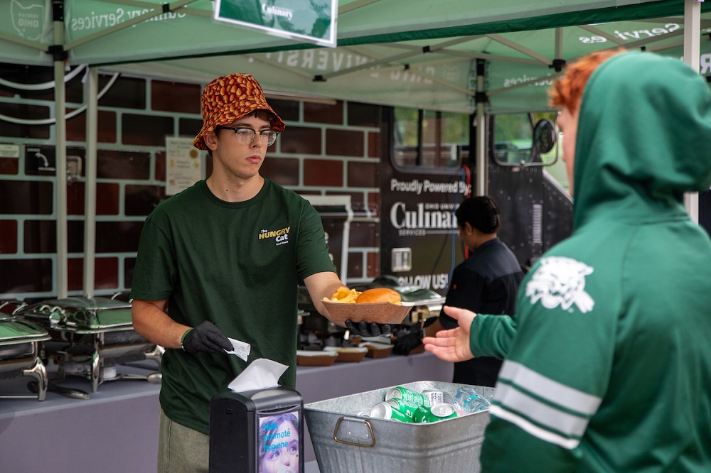 A Hungry Cat employee passes food to a customer in the tailgate area before the game.