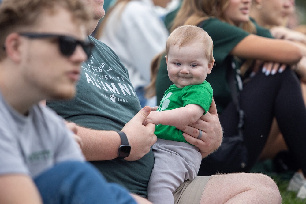An OHIO fan holds a baby dressed in green in Peden Stadium