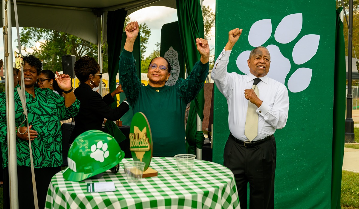 President McDavis and Deborah McDavis raise their hands to the crowd while standing in front of an OHIO pawprint sign at the dedication ceremony for the new residence hall