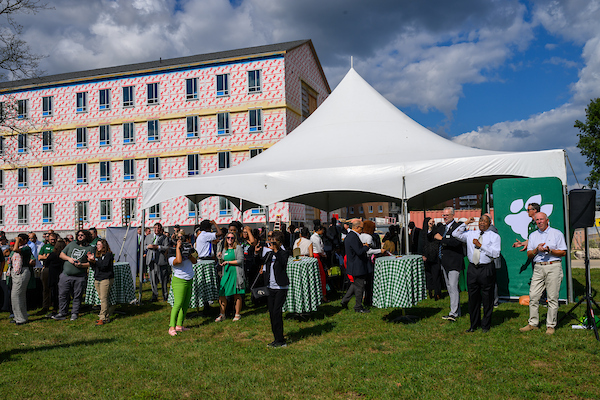 The dedication ceremony is shown in a tent in front of the new residence hall, which is under construction