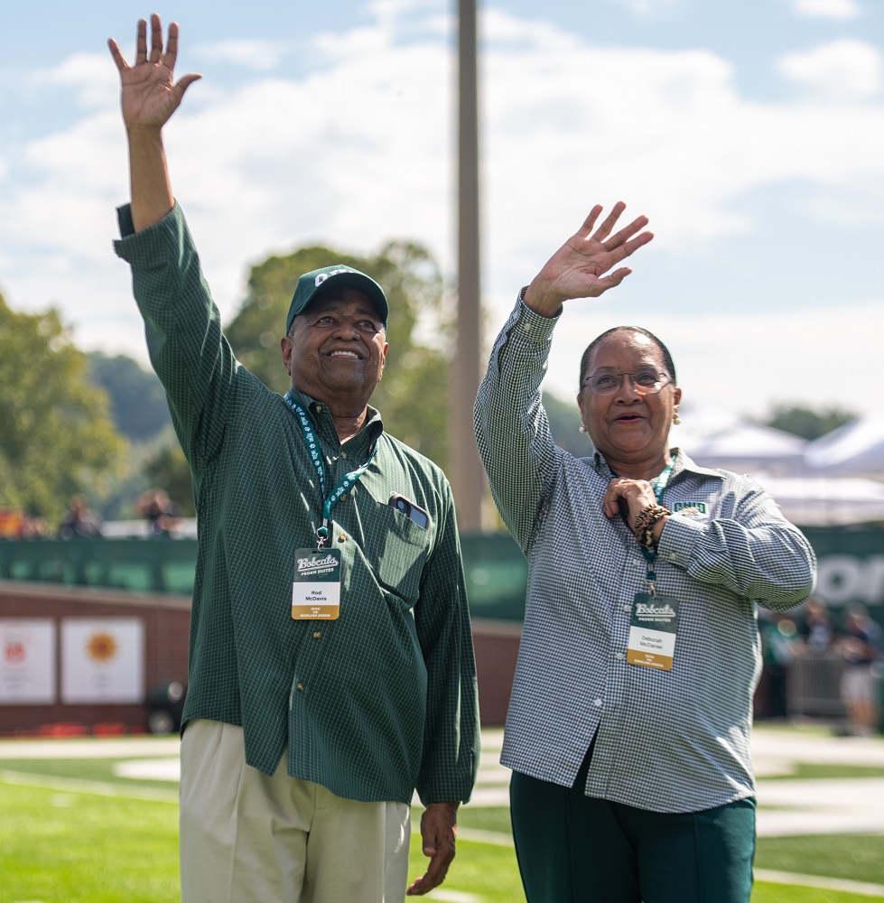 President McDavis and Deborah McDavis wave to the crowd in Peden Stadium while standing on the field during a break in action at the OHIO Football game.
