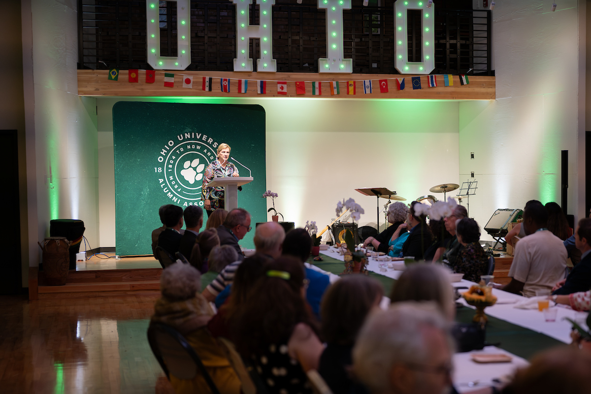 President Lori Stewart Gonzalez speaks before a large crowd, and underneath international flags and the word OHIO at the SISAL Dinner