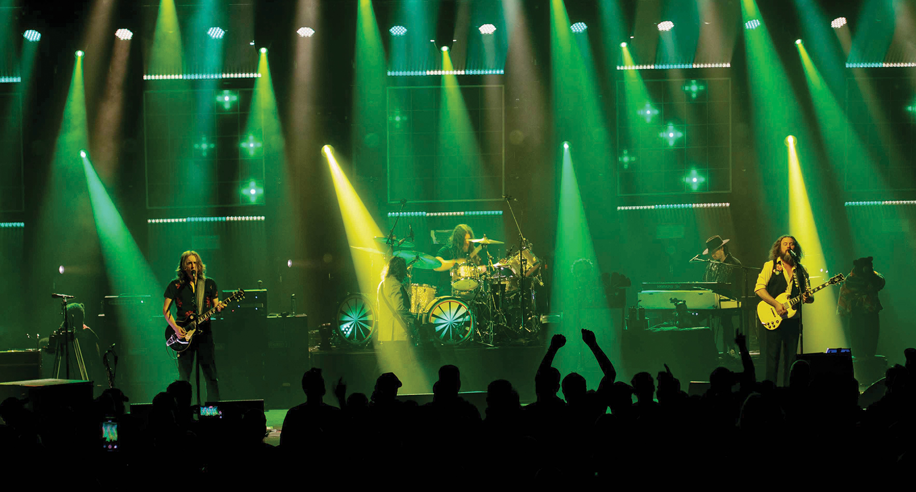  members of the band My Morning Jacket perform on stage surrounded by green and yellow lighting