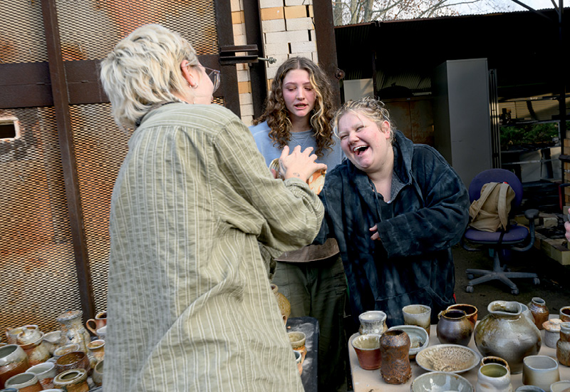 two students laugh and smile as a third holds up a finished ceramic piece