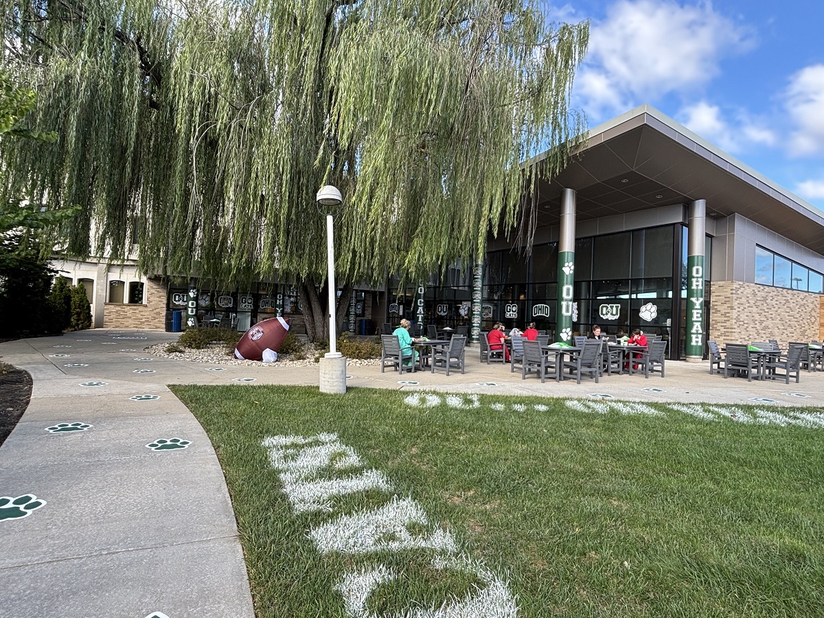 The outside of OhioHealth O'Bleness Hospital is decorated with signs that say OU, Oh Yeah and Go Cats, and the grass and sidewalks have OHIO decorations. In addition, there is a giant football under a tree.