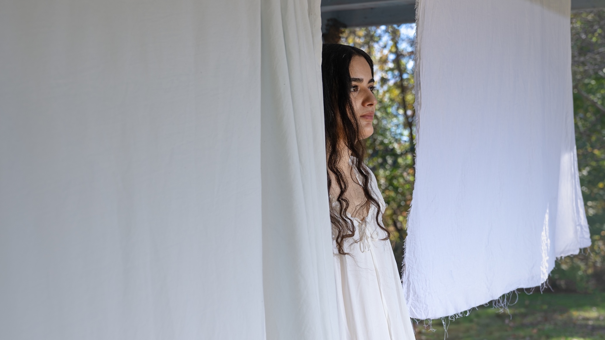 a woman sitting on her porch, with her hair pinned to a clothesline alongside some laundry 