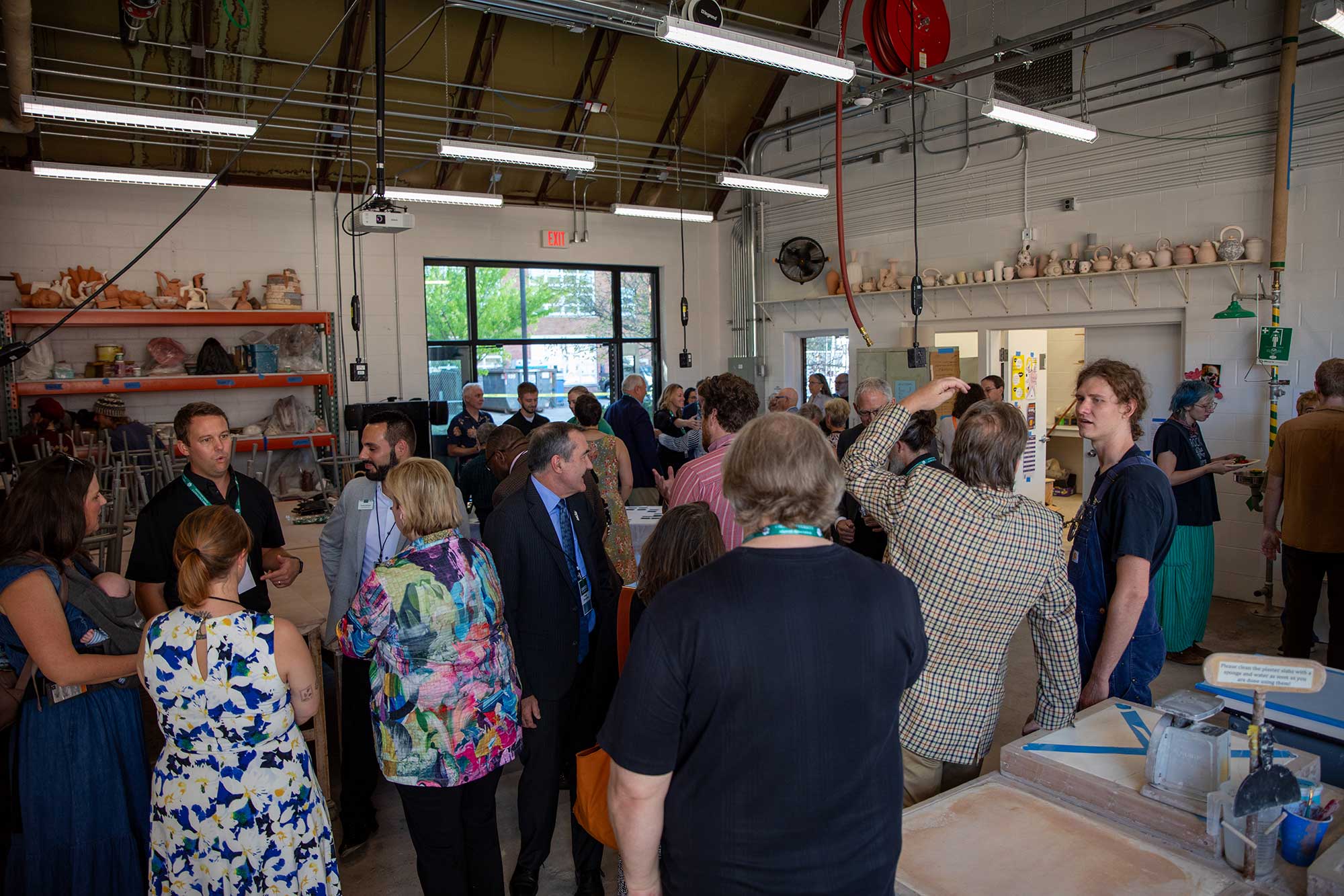 a crowd of students and adults converse in small groups in a large warehouse-like studio space