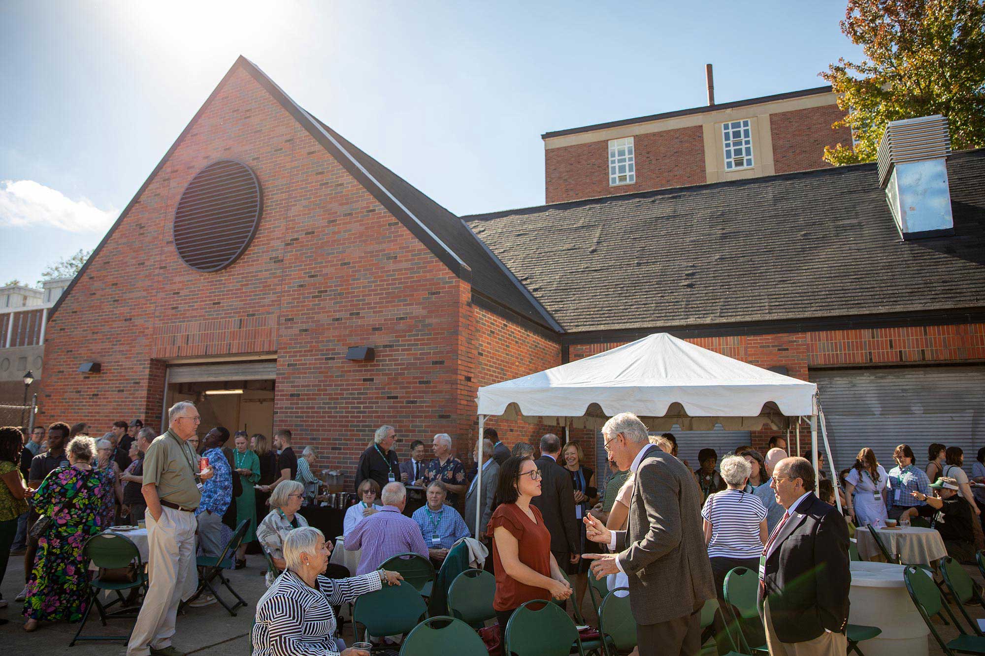 exterior photo of a small crowd conversing in small groups next to a brick building