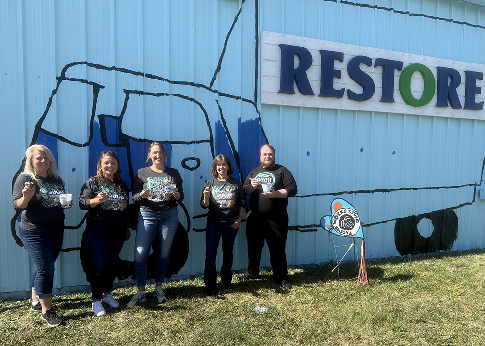 OUCU employees stand in front of a mural painted on the ReStore building