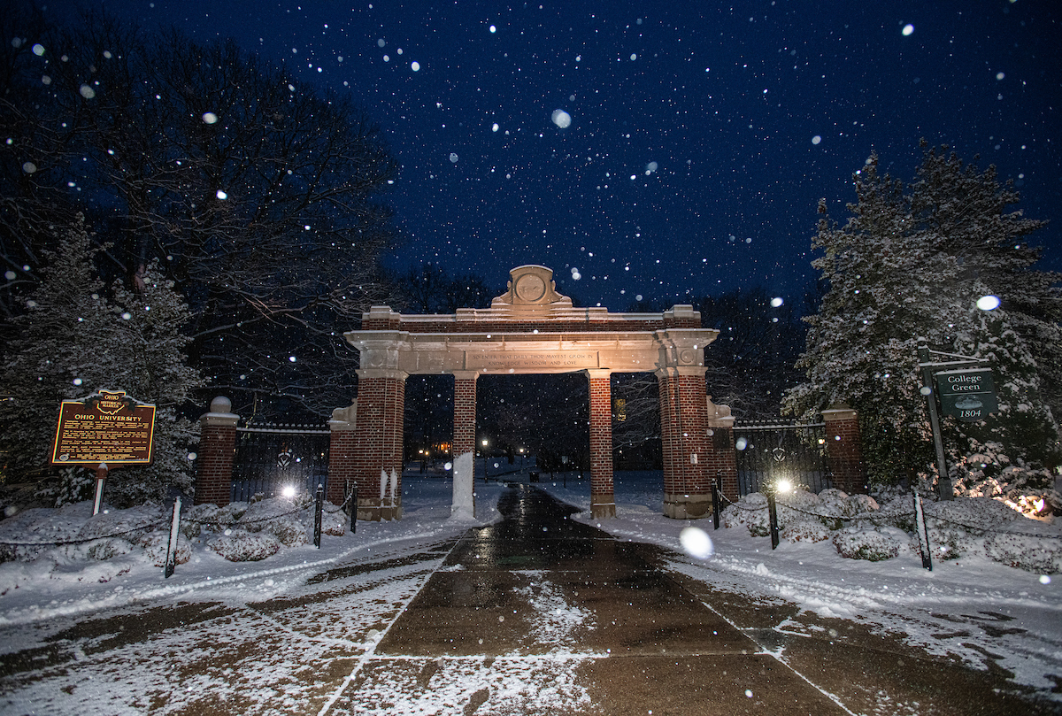 Snow falls on Alumni Gateway at night
