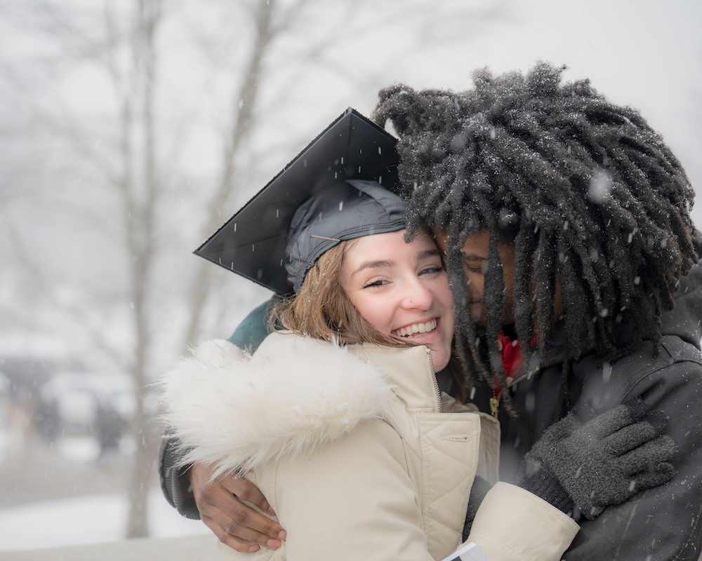 A new graduate receives a hug in the snow outside the Convo