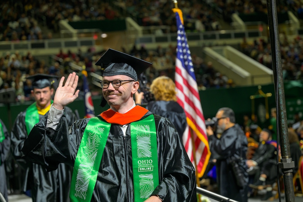 A new graduate waves from the procession