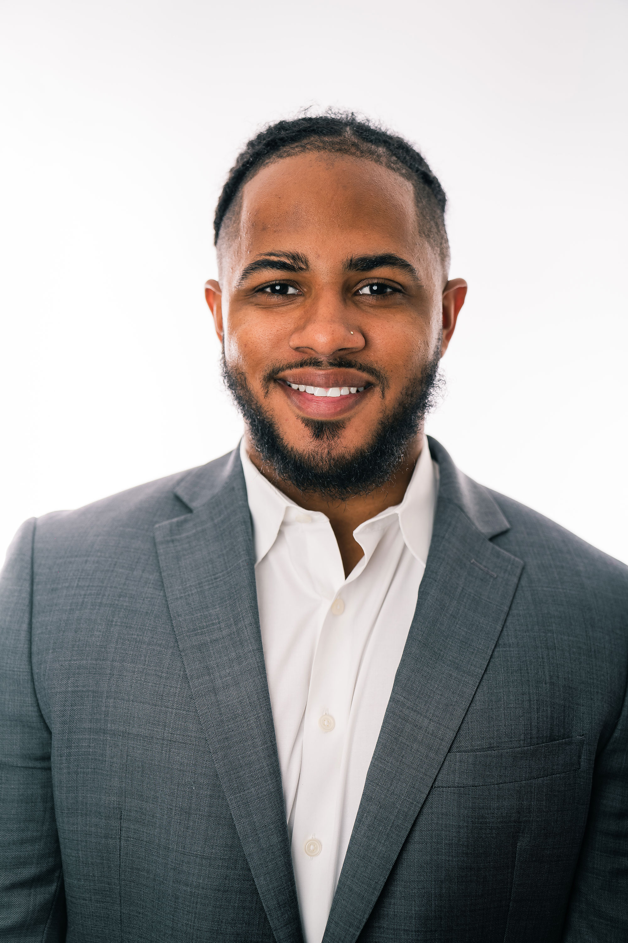 a Hispanic man with short black hair and a beard and mustache wearing a gray suit and white oxford shirt