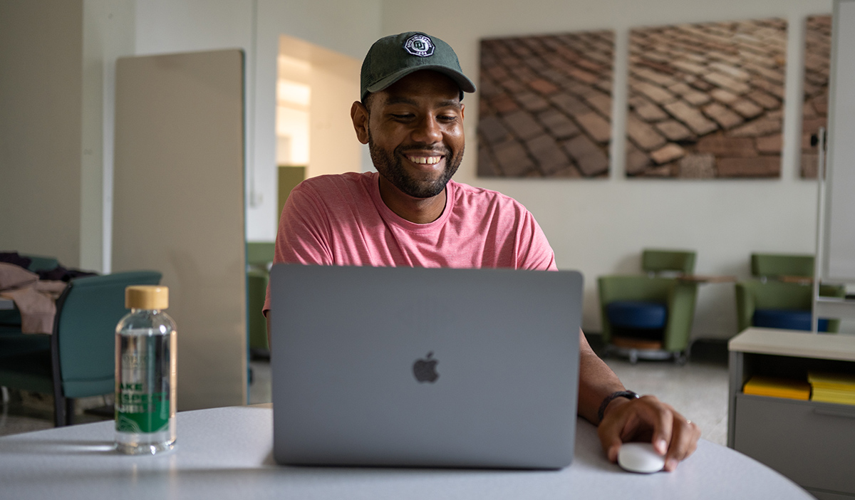 Smiling student works at a computer while sitting at a table
