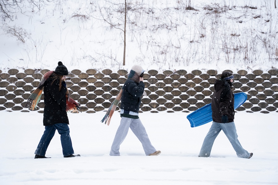 Three people walk in single-file across a snowy campus