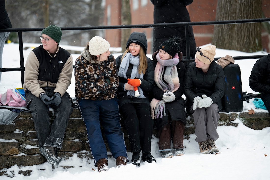 A group of students sits together in the snow, laughing