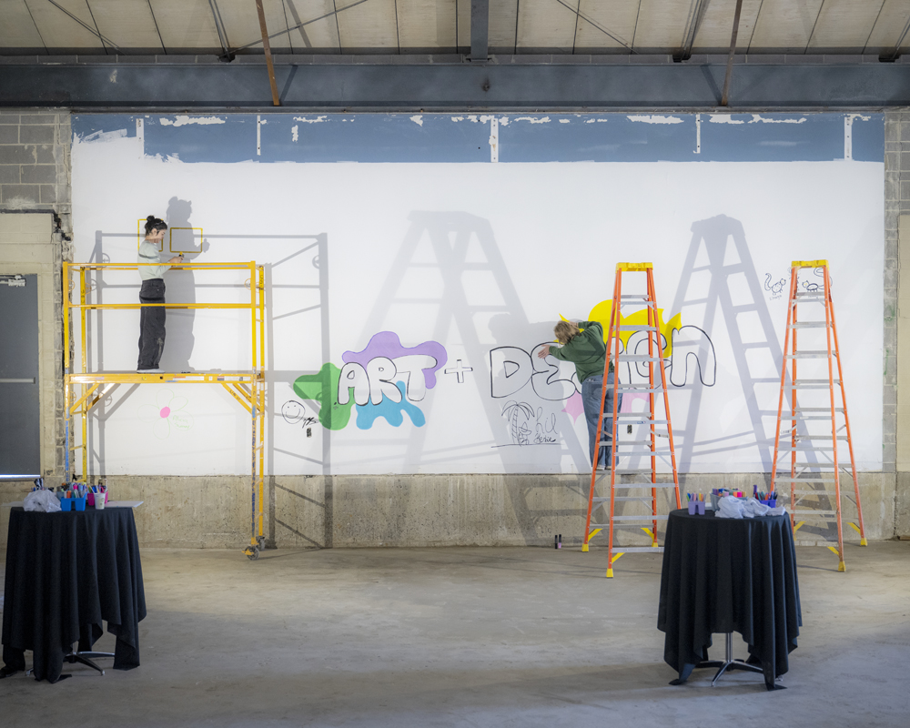 Two artists painting on the walls of Seigfred hall while its under construction