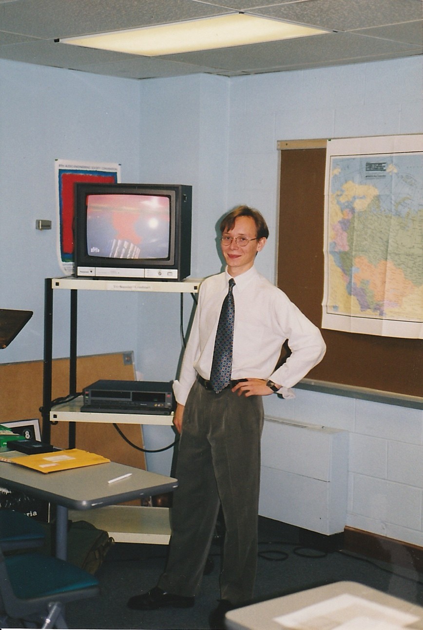An old photo of Butorin standing next to a tv atop a cart in a classroom 